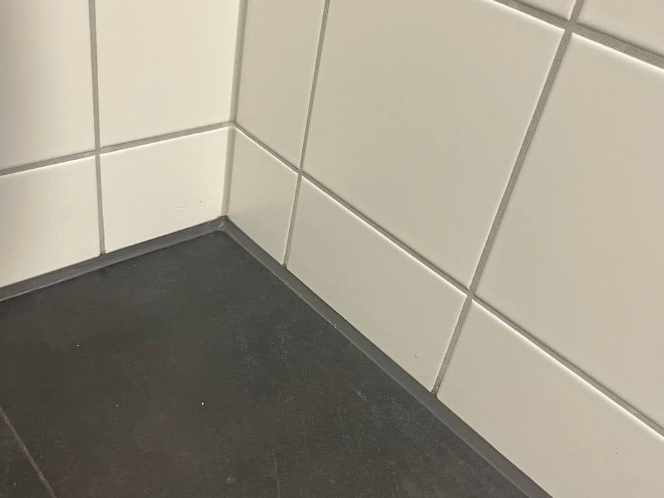 Silikonfuge in der Ecke eines Bads zwischen weißen Wandfliesen und dunklem Fliesenboden