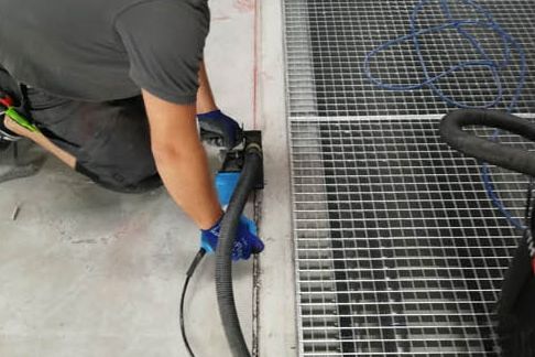 Fugenschneiden mit Absaugung neben Gitterrosten in einer Halle
