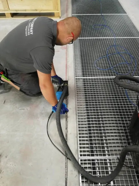 Fugenschneiden mit Absaugung neben Gitterrosten in einer Halle